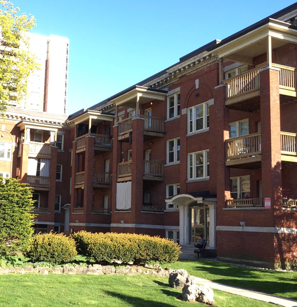 South wing of the Hampton Court apartments, Hamilton, with three sets of balconies, seen on a sunny spring day, landscaping and large stones in the foreground