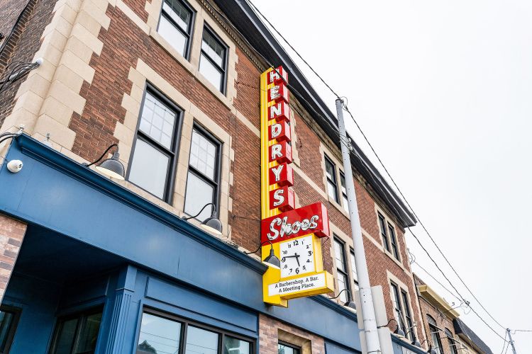 Closeup of the Hendry's building with refurbished neon sign (including clock) reading HENDRYS Shoes: A Barbershop. A Bar. A Meeting Place.